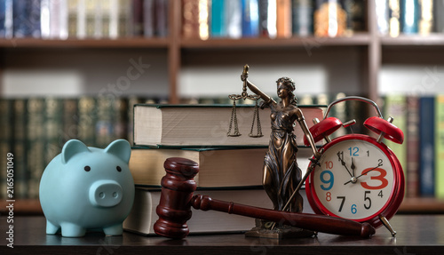 A blue piggy bank, a judge's gavel, and a figure of Themis against a backdrop of bookshelves.