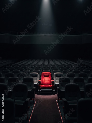 Single Red Seat Illuminated in a Dark Empty Movie Theater Auditorium with Spotlight.