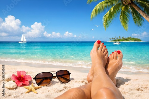 Tropical beach vacation background featuring woman feet relaxing on white sand with sunglasses, seashell, hibiscus flower and palm tree. summer vacation concept.