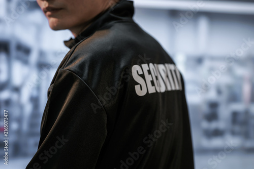 фотографія Close view of a security guard wearing a black jacket with security lettering, standing indoors in a blurred public building