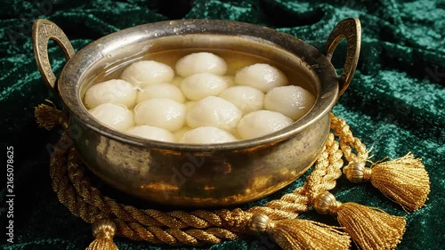 Traditional Rasgulla in vintage metallic bowl on green velvet fabric with golden tassels for Mawlid celebration, festive dessert arrangement for religious holiday dining