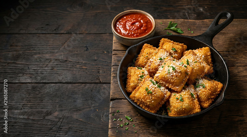 Golden toasted ravioli in skillet with marinara sauce on dark wooden table
