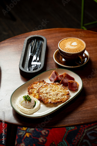 Delicious breakfast spread with crispy potato cake, bacon, and a cozy coffee at a warm cafe