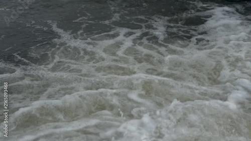 Intense close-up of fast river rapids creating bubbling white foam over dark rushing water. Powerful natural fluid motion representing raw hydro energy.