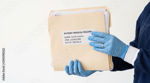 Medical professional hands wearing blue latex gloves holding beige patient medical record folder with identification label, confidential healthcare documentation