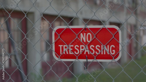 Close-up of a barbed wire fence with a no trespassing sign on a metal chain fence (slow tilt down)