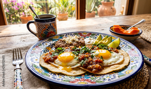 A rich plate of classic Huevos Rancheros served on a vintage floral Talavera ceramic plate, Two sunny-side-up fried eggs with golden runny yolks resting on lightly fried corn tortillas, smothered in w