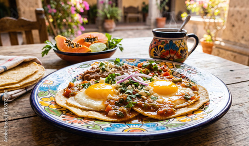 A rich plate of classic Huevos Rancheros served on a vintage floral Talavera ceramic plate, Two sunny-side-up fried eggs with golden runny yolks resting on lightly fried corn tortillas, smothered in w