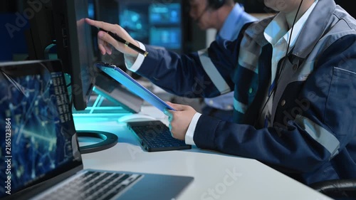 Asian engineer in headset analyzes radar screens and takes notes in a high-tech control room, managing telemetry