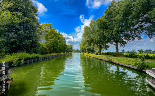 long canal leading toward distant horizon with guiding posts and vivid sky. strong linear composition, calm water lanes, framed