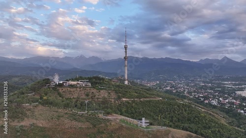The famous TV tower on Kok Tobe Mountain in the Kazakh city of Almaty, set against a mountain range on a cloudy summer evening.