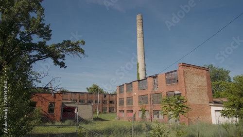 Extreme wide shot of an abandoned factory made of brick with a towering smokestack (tilt up)