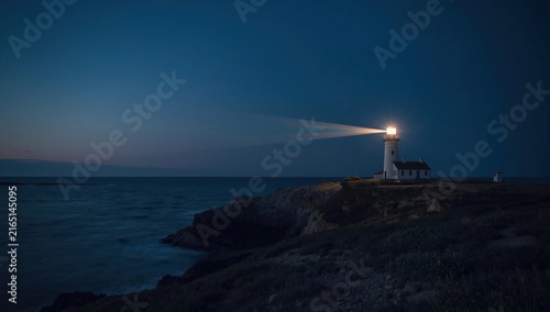 Lighthouse illuminating the ocean at dusk with a clear sky and calming waves, coastal scene