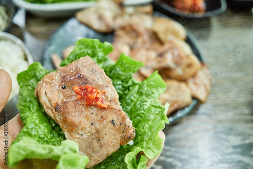 Fotografie Hand holding a fresh green lettuce wrap with grilled meat and spicy paste