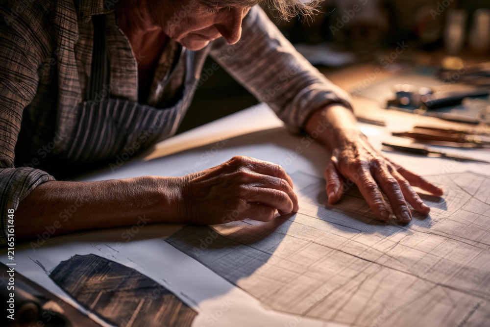 Fototapeta premium Warm light bathes an artisan's hands on detailed blueprints