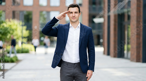 Man in business suit saluting outdoors during daytime with urban buildings in background