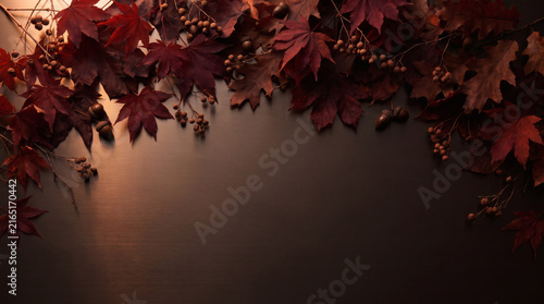 Dark burgundy autumn leaves background with acorns branches and warm copy space for product display
