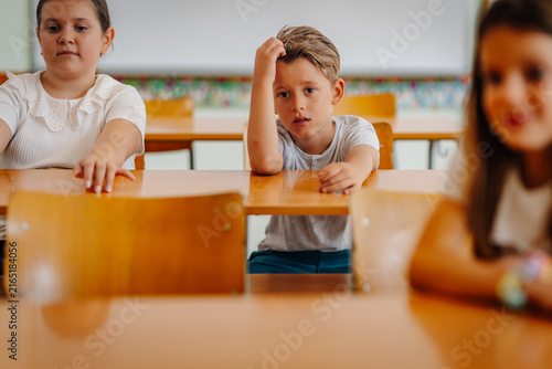 Fototapeta Elementary student sitting at desk looking thoughtful having difficulty learning
