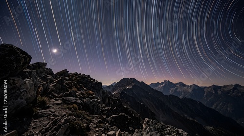 Star trails arc beautifully over a rocky mountain range at night.