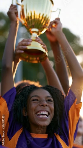 Smiling young soccer player holding championship trophy aloft at golden hour celebrating triumph for sports poster and background