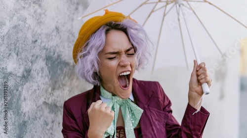 Young woman with purple hair yelling under umbrella urban fashion portrait for editorial background and dramatic expression