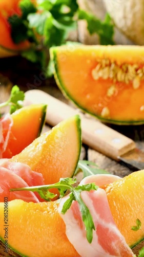 Fresh melon slices with prosciutto ham and arugula on wooden board, vertical footage
