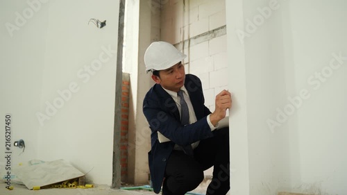 Construction inspector wearing safety helmet conducts thorough examination of unfinished building wall with exposed bricks and construction materials ensuring safety and project development indoors