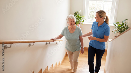 Elderly woman practicing stair climbing with assistance from caregiver in bright home setting, showing support and care