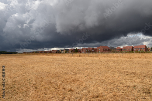 After months of drought in storm clouds gather over a new housing estate  rain relive over due on grass and countryside 
