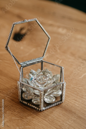 Gold wedding rings for the bride and groom on their wedding day in a transparent box of an unusual shape decorated with various precious stones lies on the table