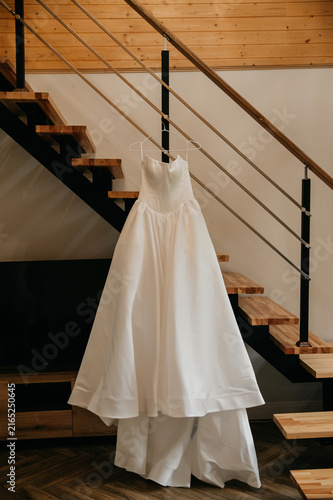 White wedding dress for the bride hanging on a trellis against the background of the stairs in a hotel room on the wedding day