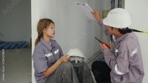 Construction inspector and worker wearing safety helmets and gear engage focused discussion and teamwork using clipboard and walkie talkie inside building construction site ensuring safety