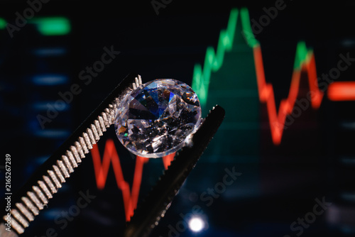 фотографія Diamond held by tweezers over fluctuating financial investment chart display