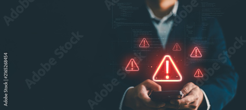 Businessman hand using smartphone with red warning triangle alert icon for cyber threat, malware attack, data breach, system error, risk assessment, fraud, security vulnerability and network virus