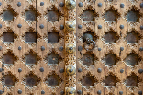 Canvastavla Close-up of a traditional carved wooden door featuring handcrafted details, metal studs and geometric floral ornamentation in Konya, Turkey