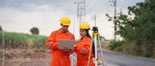 Civil engineers and survey team using a total station theodolite and road construction plans to measure and map out a construction site
