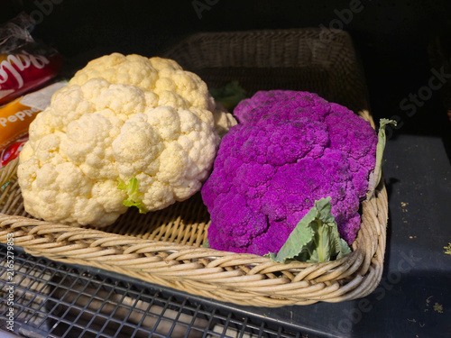 Two colorful cauliflower heads, white and purple, displayed in a woven basket