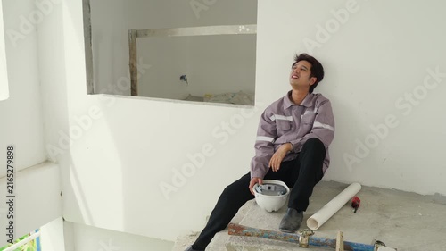Construction inspector takes break sitting concrete floor inside unfinished building holding safety helmet resting against white wall calm moment with worker indoor building site safety equipment