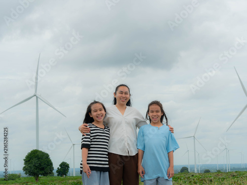 Obraz na plátne Smiling Asian mother hugging her two happy daughters in front of wind turbines
