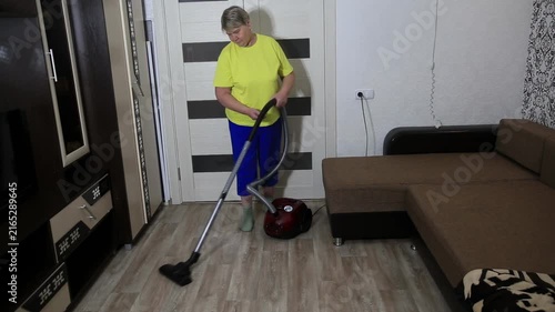Adult woman performing household chore of cleaning floor with red vacuum cleaner in bright room of home, diligently vacuuming during day, maintaining cleanliness.