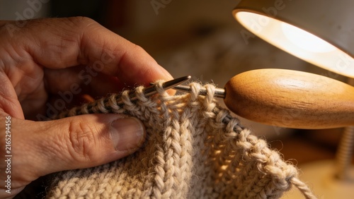 Close-up of hands darning a wool sock with a wooden darning egg under warm lamp light