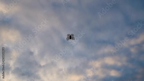 Drone flying against a dramatic sunset sky filled with colorful clouds, viewed from below. Cinematic low-angle view of a camera drone silhouetted against the evening sky
