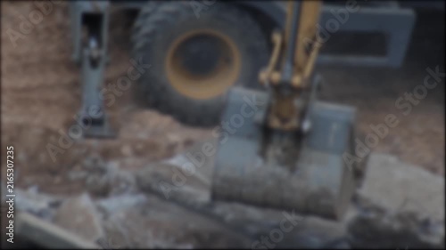 Excavator bucket breaking concrete slabs and moving earth at construction site. Heavy machinery operation during demolition, ground preparation, and civil engineering work, blurry, copy space