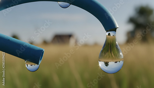 Detailed view of water droplets resting on a blue garden hose with a softly blurred backdrop of tall grass and an indistinct house showcasing the tranquility of nature