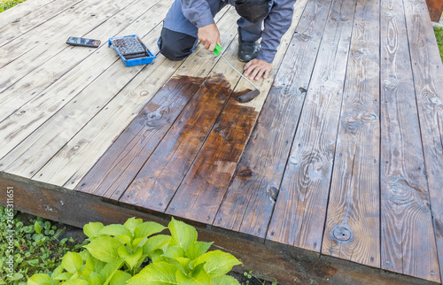 Bild auf Leinwand Worker cleans wooden patio, revealing fresh finish after staining