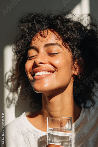 Woman with eyes closed and a radiant smile drinks water from a glass