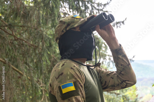 Foto Camouflaged soldier scanning distant landscape with binoculars in forest