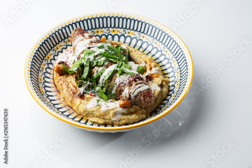 Bild auf Leinwand Grilled meat kofta served over creamy hummus with herbs, nuts and white sauce