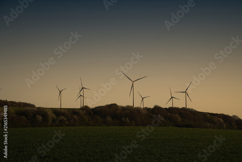 Wind turbines as silhouettes on a hill at twilight.