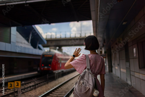 Summer trip. A cheerful young female traveler waves to her friends at the train station. Meeting up with friends. A young woman at the station.